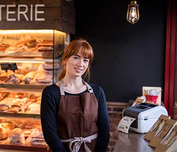 Femeie purtând șorț maro în cafenea cu sandvișuri și imprimantă de etichete TD pe masă