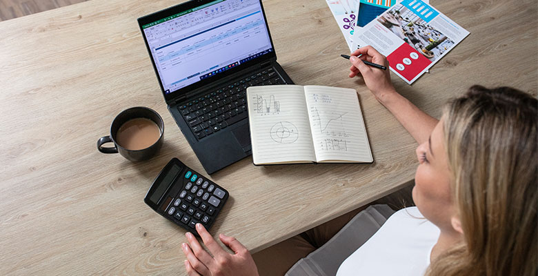 Vedere de sus a unei femei cu laptop, blocnotes, cană de cafea și calculator pe birou din lemn