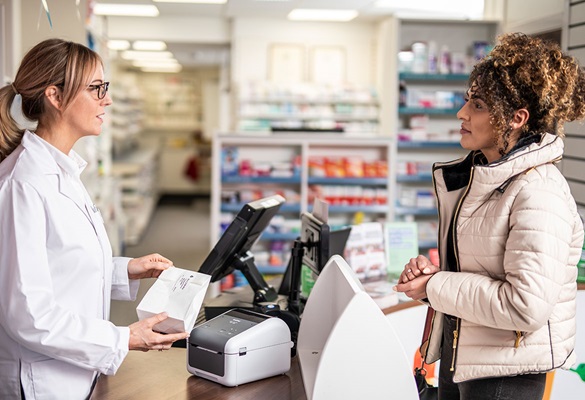 Farmacistă servind o clientă, imprimantă de etichete pe masă